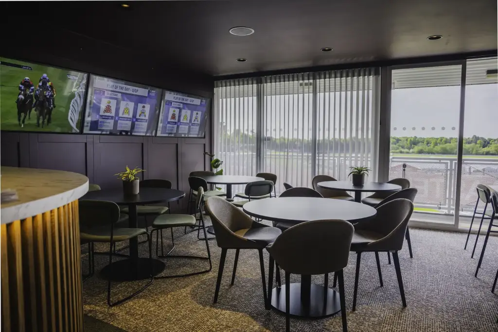 A private box with round tables, a curved bar and windows over the racecourse