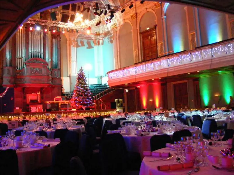 Concert Hall set for a Christmas dinner with round tables, a tree on the stage and coloured lighting