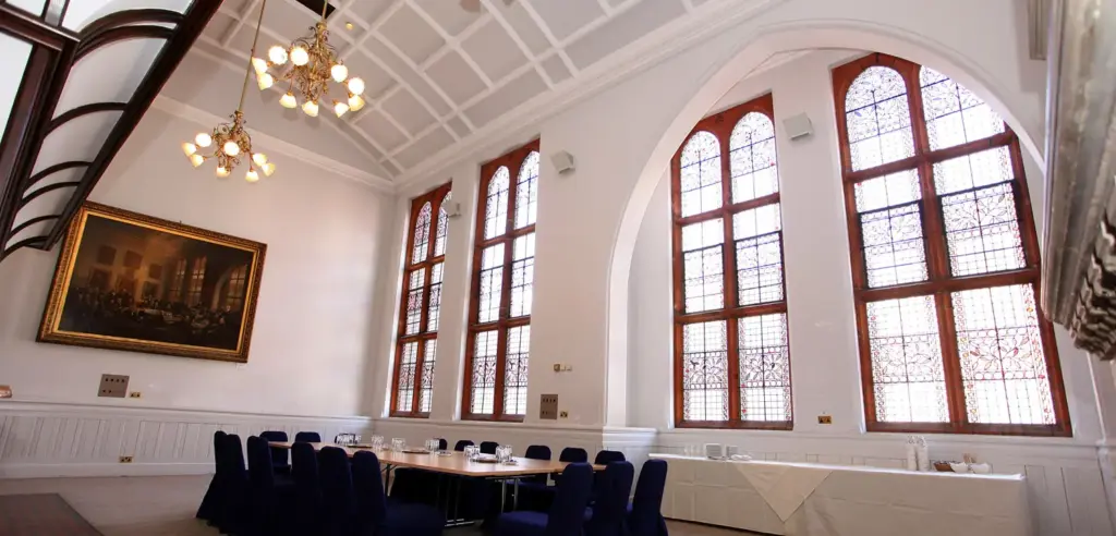 Waterhouse Chamber set as a boardroom beneath tall arched stained glass windows