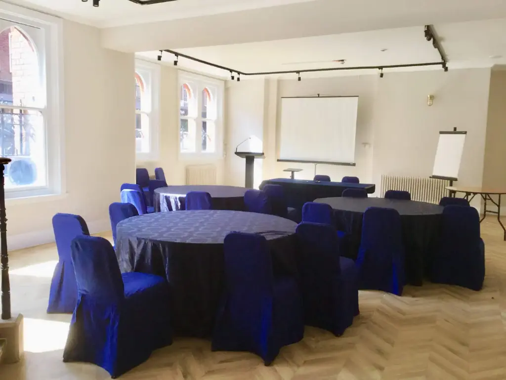 Soane Space with round tables in blue covers, a projection screen and flip chart